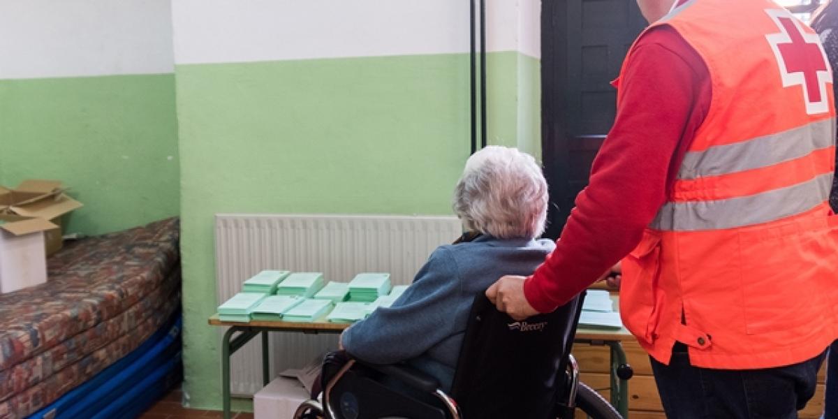 Un voluntario de Cruz Roja Española con un mayor votando.